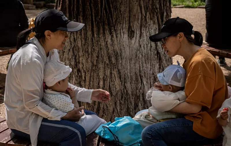 Two women and two babies sit on a bench in a park in Beijing on May 25, 2021. (Photo by NICOLAS ASFOURI / AFP)
