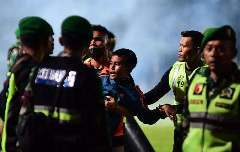 This picture taken on October 1, 2022 shows a boy (C) being carried as members of the Indonesian army secure the pitch after a football match between Arema FC and Persebaya Surabaya at Kanjuruhan stadium in Malang, East Java. - At least 127 people died at a football stadium in Indonesia late on October 1 when fans invaded the pitch and police responded with tear gas, triggering a stampede, officials said. (Photo by AFP)