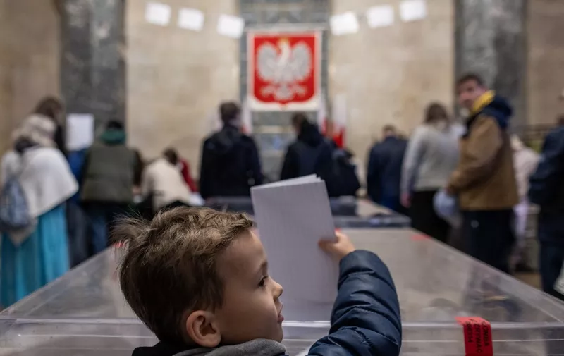 A child casts a parent's vote in the polling station at the Palace of Culture in Warsaw, Poland on October 15, 2023, during parliamentary elections. Poles are voting with the ruling populists hoping to win a third term in power by defeating the liberal opposition led by former EU chief Donald Tusk. (Photo by Wojtek RADWANSKI / AFP)