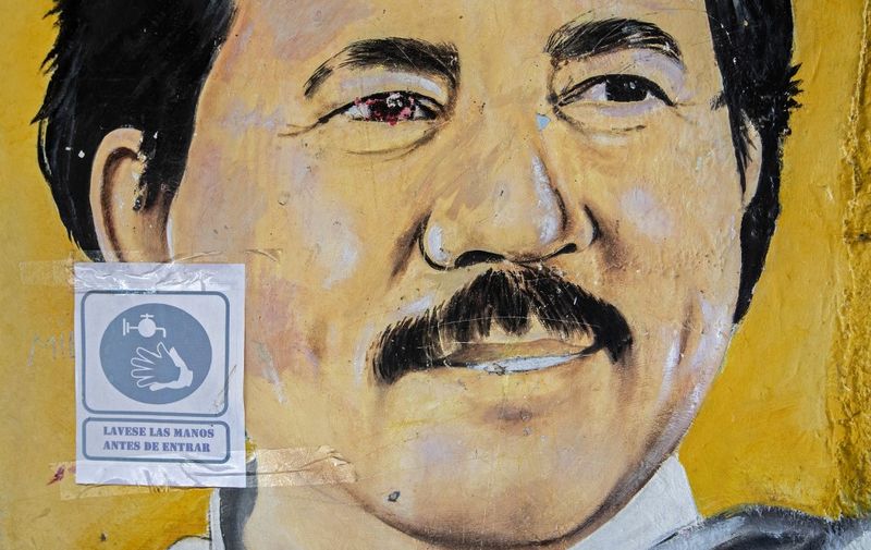 A sign reading "Wash your hands before entering" remains pasted on a mural depicting Nicaraguan President Daniel Ortega at the Sandinista National Liberation Front (FSLN) headquarters in Catarina, Nicaragua, on July 17, 2020, amid the new coronavirus pandemic. - Nicaragua will celebrate on Sunday the 41st anniversary of the Sandinista Revolution, for the first time without a public event for the speech of Nicaraguan President Daniel Ortega due to the COVID-19 pandemic. (Photo by INTI OCON / AFP)