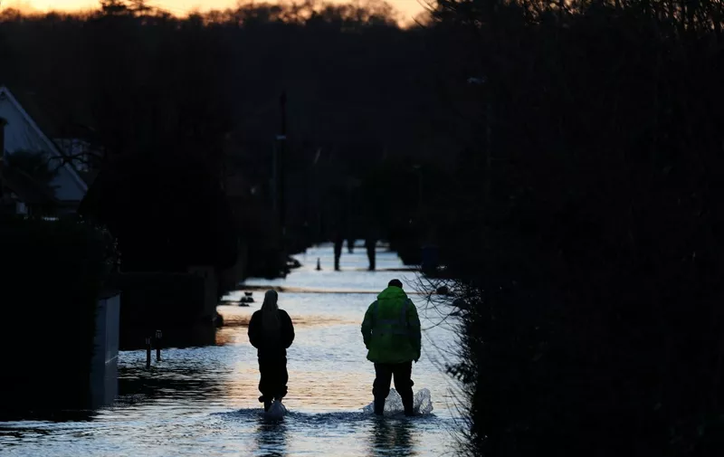 People walk through floodwater on a flooded street in Wraysbury, west of London on January 9, 2024, after heavy rain brought flooding to much of the country following Storm Henk. (Photo by Daniel LEAL / AFP)
