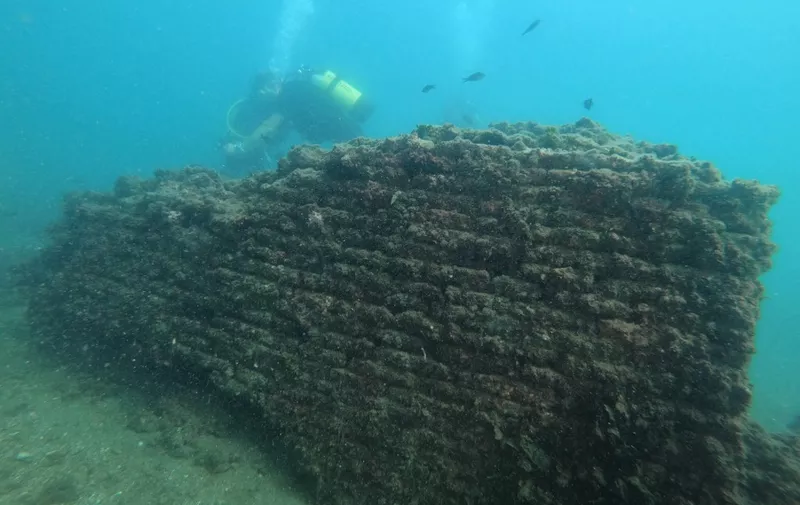 In this photograph taken on August 18, 2021 a dive guide shows tourists a Roman brick wall of the thermal building of the Nymphaeum of punta Epitaffio, the submerged ancient Roman city of Baiae at the Baiae Underwater Park, part of the Campi Flegrei Archaeological Park complex site in Pozzuoli near Naples. Statues which once decorated luxury abodes in this beachside resort are now playgrounds for crabs off the coast of Italy, where divers can explore ruins of palaces and domed bathhouses built for emperors. (Photo by Andreas SOLARO / AFP)