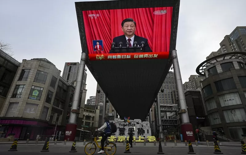 An outdoor screen shows a live news coverage of Chinas President Xi Jinping delivering a speech during the closing session of the National People's Congress (NPC) at the Great Hall of the People, along a street in Beijing on March 13, 2023. (Photo by JADE GAO / AFP)