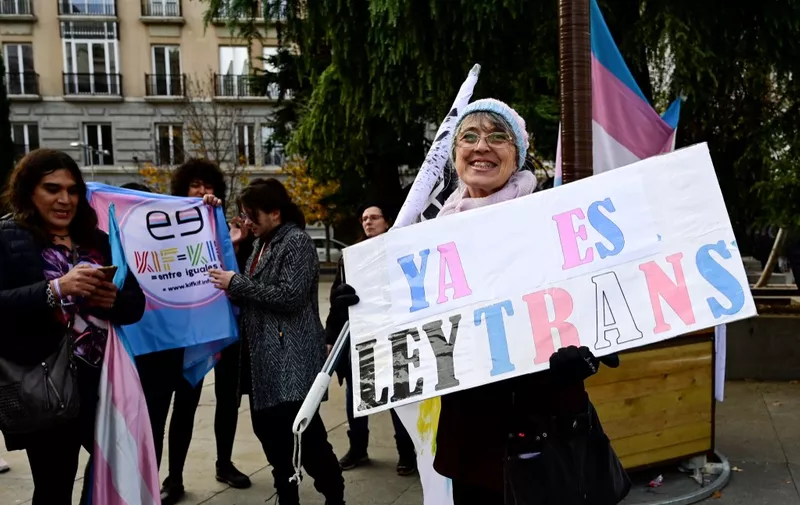 A demonstrator holds a sign reading "It's a law now" as activists gather to celebrate after a vote in favour of a transgender rights bill in front of the Spanish Congress of Deputies in Madrid, on December 22, 2022. - Spanish lawmakers passed a transgender rights bill allowing anyone 16 and over to change gender on their ID card, legislation that has divided Spain's left-wing government and its feminist movement. Approved by 188 votes in favour to 150 against and seven abstentions, the bill now moves to the Senate where, if left unchanged as expected, it will become law within weeks. The move will make Spain one of the world's few countries to allow transgender people to change their status with a simple declaration. (Photo by JAVIER SORIANO / AFP)