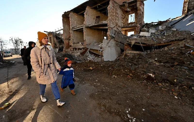 A local resident hold the hand of a child as they walk past a destroyed building following a C-300 missile strike on the Ukrainian city of Kharkiv on March 31, 2023. (Photo by SERGEY BOBOK / AFP)