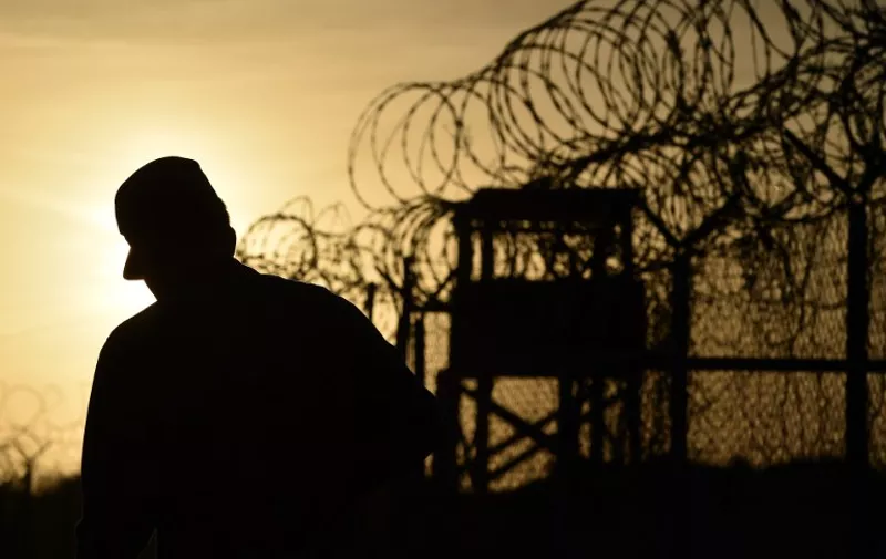 This photo made during an escorted visit and reviewed by the US military, shows an US soldier walking next to the razor wire-topped fence at the abandoned "Camp X-Ray" detention facility at the US Naval Station in Guantanamo Bay, Cuba, April 9, 2014.   AFP PHOTO/MLADEN ANTONOV / AFP / MLADEN ANTONOV