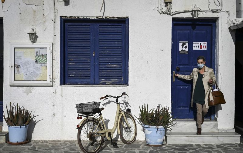 A woman wearing a face mask leaves a building in the small southern Greek island of Elafinissos on April 23, 2021. - Greece is full steam ahead at vaccinating dozens of small islands under one thousand inhabitants in the Aegean and Ionian Sea that will be labelled as "covid - free islands" ahead of the official opening of the tourist season on May 14. 610 residents of Elafonissos islands, famous for its sandy beaches and dunes, have already received at least one Covid jab with almost two thirds of the island's population receiving their second dose on Friday. (Photo by ARIS MESSINIS / AFP)