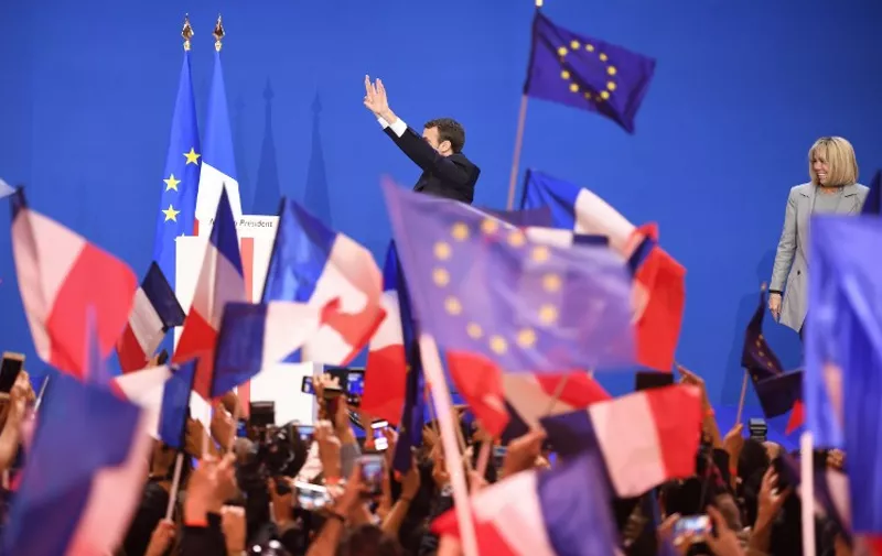 French presidential election candidate for the En Marche ! movement, Emmanuel Macron (C) waves at supporters as his wife Brigitte Trogneux (R) looks on, on stage at the Parc des Expositions in Paris, on April 23, 2017, after the first round of the Presidential election.
Pro-European Emmanuel Macron is set to face far-right candidate Marine Le Pen in France's presidential run-off, results showed on April 24, making him clear favourite to emerge as the country's youngest leader in its history. / AFP PHOTO / Eric FEFERBERG