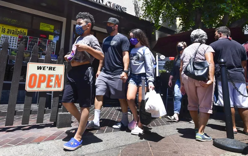 Face masks continue to be worn as people walk past restaurants open for business in Los Angeles on June 14, 2021, one day before the state full reopening of its economy since the first statewide shutdown in March 2020 due to the coronavirus pandemic. - California is removing nearly all pandemic restrictions on June 15, with no mandatory capacity restrictions or social distancing requirements for those who have been vaccinated. (Photo by Frederic J. BROWN / AFP)