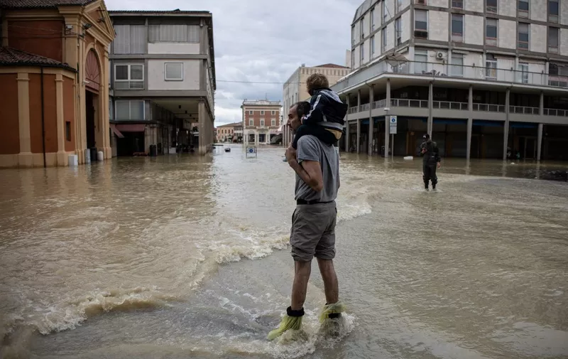 A resident carries a child in a flooded street in the town of Lugo on May 18, 2023, after heavy rains caused flooding across Italy's northern Emilia Romagna region. Rescue workers searched on May 18, 2023 for people still trapped by floodwaters in northeast Italy as more residents were evacuated after downpours which killed nine people and devastated homes and farms. (Photo by Federico SCOPPA / AFP)