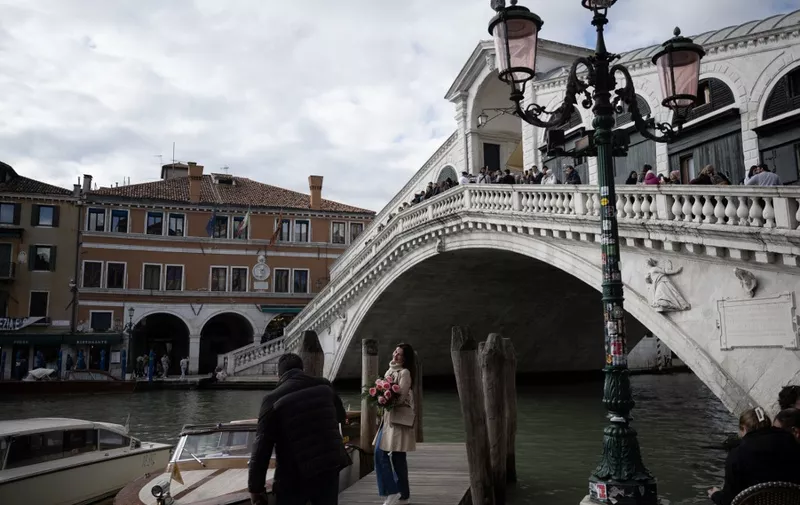 A woman poses with a flower bouquet in front of the Rialto Bridge on April 24, 2024 in Venice, on the eve of the start of the official trial of the city's booking system for day-trippers. Venice will begin on April 25, 2024 charging day trippers for entry, a world first aimed at easing pressure on the Italian city drowning under the weight of mass tourism. (Photo by MARCO BERTORELLO / AFP)
