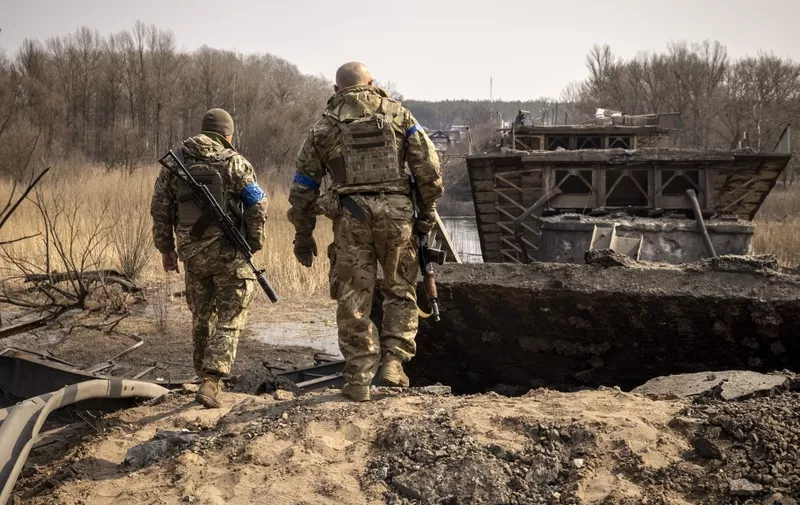 Ukrainian soldiers patrol near a bridge destroyed by the Russian army in the town of Rogan, east of Kharkiv, on March 30, 2022. - Ukrainian forces on March 28, 2022 recaptured a small village on the outskirts of Ukraine's second-largest city Kharkiv, as Kyiv's forces mount counterattacks against a stalling Russian invasion. Members of the Ukrainian army were clearing and securing destroyed homes in the settlement of Mala Rogan, about five kilometres (three miles) from Kharkiv, after pushing out Russian forces. (Photo by FADEL SENNA / AFP)