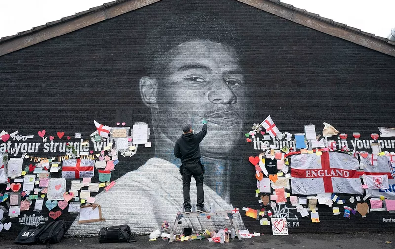 Street artist Akse P19 repairs the mural of Manchester United striker and England player Marcus Rashford on the wall of the Coffee House Cafe on Copson Street, in Withington, Manchester, England, Tuesday July 13, 2021. The mural was defaced with graffiti in the wake of England losing the Euro 2020 soccer championship final match to Italy, but subsequently covered with messages of support by well wishers. (AP Photo/Jon Super)