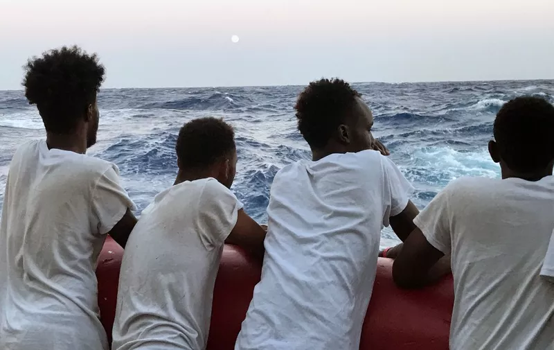 Rescued migrants look at the sea as they stand on the deck of 'Ocean Viking' rescue ship, operated by French NGOs SOS Mediterranee and Medecins sans Frontieres (MSF) on August 14, 2019, during a search-and-rescue operation in the Mediterranean Sea. - French charities SOS Mediterranea and MSF rescued another 105 migrants off the coast of Libya on August 12, bringing to 356 the number of those aboard the Ocean Viking now seeking a safe port. The rescues come at a time of tension between Italy and other EU states, with Rome refusing to let migrants land on its shores unless its EU partners shoulder their share of the burden. The UN refugee agency UNHCR has asked European governments to allow the migrants aboard the Ocean Viking, as well as 150 others aboard the Spanish rescue boat Open Arms waiting off the coast of Lampedusa, to disembark. (Photo by Anne CHAON / AFP)