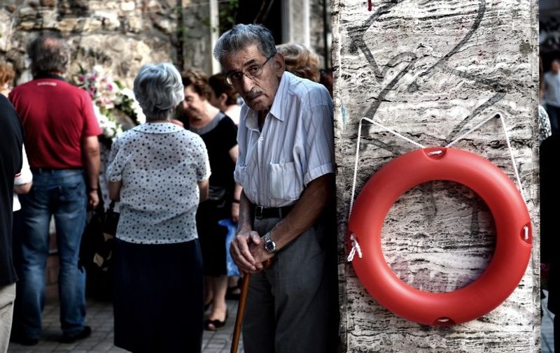 An elderly man stands beside a lifebuoy hanging on a wall outside a chapel in central Athens on July 7, 2015.  Eurozone leaders will hold an emergency summit in Brussels on July 7 to discuss the fallout from Greek voters' defiant "No" to further austerity measures, with the country's Prime Minister Alexis Tsipras set to unveil new proposals for talks.  AFP PHOTO / ARIS MESSINIS