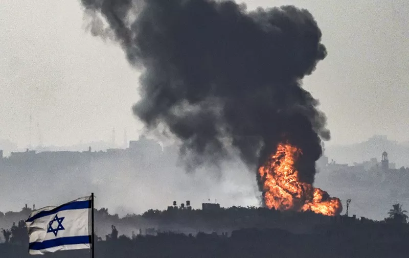 An Israeli flag flies at a position in southern Israel while across the border in the Gaza Strip a fireball erupts during Israeli bombardment on November 8, 2023 amid ongoing battles between Israel and the Palestinian Hamas movement. (Photo by RONALDO SCHEMIDT / AFP)