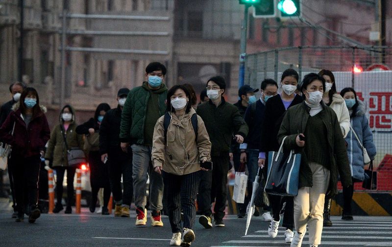 People wearing protective facemasks cross a street in Shanghai on February 25, 2020. - The new coronavirus has peaked in China but could still grow into a pandemic, the World Health Organization warned, as infections mushroom in other countries. (Photo by NOEL CELIS / AFP)