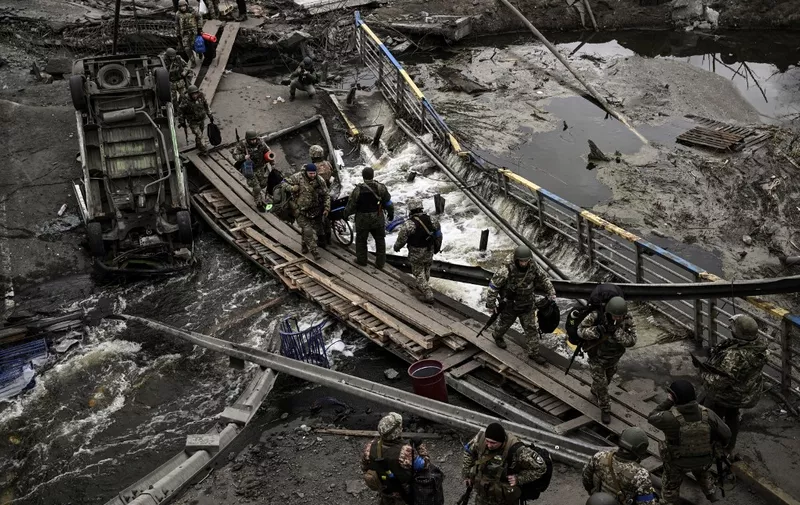 Ukranian servicemen walk on a makshift pathway to cross a river next to a destroyed bridge near the city of Irpin, northwest of Kyiv, on March 13, 2022. Russian forces advance ever closer to the capital from the north, west and northeast. Russian strikes also destroy an airport in the town of Vasylkiv, south of Kyiv. A US journalist was shot dead and another wounded in Irpin, a frontline northwest suburb of Kyiv, medics and witnesses told AFP. (Photo by Aris Messinis / AFP)