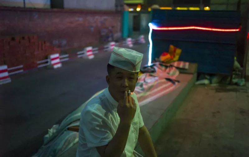 A cooker smokes a cigarette in the street on May 27, 2015 in Beijing. China's capital seeks to snuff indoor smoking on June 1st, 2015 with a new ban and unprecedented fines.  AFP PHOTO / FRED DUFOUR