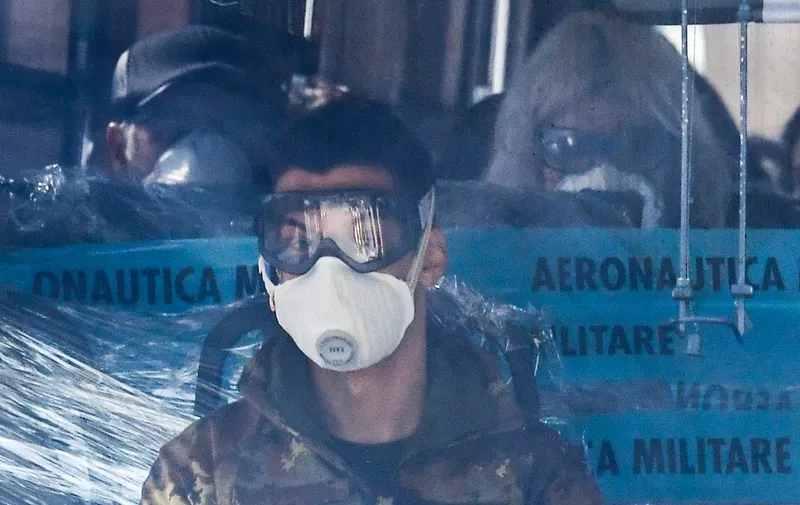 A military personnel (Front) sits in coach transporting Italian citizens (Rear) repatriated from the coronavirus hot-zone of Wuhan, leaves the Mario De Bernardi military airport in Pratica di Mare, south of Rome, on February 3, 2020 after landing from China, to be placed in quarantine at the nearby Cecchignola center. (Photo by Andreas SOLARO / AFP)