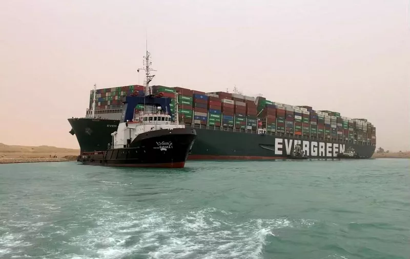 A handout picture released on March 24, 2021 shows the Taiwan-owned MV Ever Given (Evergreen), a 400-metre- (1,300-foot-)long and 59-metre wide vessel, lodged sideways and impeding all traffic across the waterway of Egypt's Suez Canal. - A giant container ship ran aground in the Suez Canal after a gust of wind blew it off course, the vessel's operator said on March 24, 2021, bringing marine traffic to a halt along one of the world's busiest trade routes. (Photo by - / Suez CANAL / AFP)