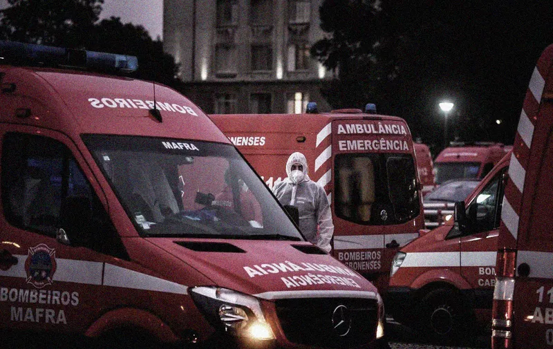 A health worker wearing a protective suit stands in the middle of dozens of ambulances waiting outside the Covid-19 emergency services of Santa Maria Hospital in Lisbon on January 28, 2021. - Portugal reported twin Covid records with 303 new deaths and 16,432 cases in a 24-hour period, prompting a decision to limit foreign travel to "special cases". (Photo by PATRICIA DE MELO MOREIRA / AFP)