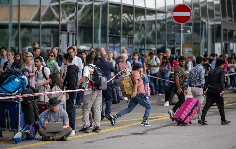 Travellers queue with luggage to enter Geneva International Airport in Geneva on June 30, 2023, amid a strike action by airport workers. Some 59 flights were cancelled at Geneva's international airport, it said, after operations were halted for four hours because of a worker's strike at the start of the busy summer travel season. (Photo by Fabrice COFFRINI / AFP)