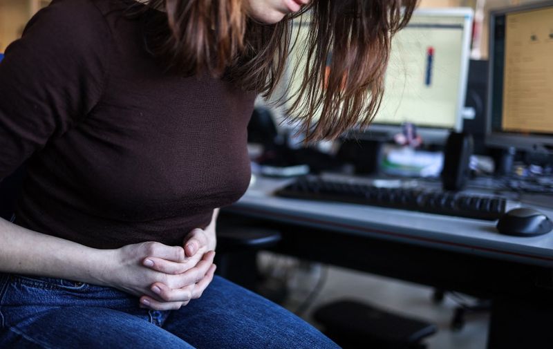 This illustration photograph taken on March 1, 2023 shows a woman with painful periods sitting on a chair while at work in Toulouse, southwestern France. (Photo by Charly TRIBALLEAU / AFP)