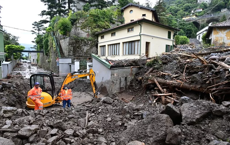 Workers stand by an excavator used to clear the damages caused by a landslide in Laglio after heavy rain caused floods in towns surrounding Lake Como in northern Italy, on July 28, 2021. (Photo by MIGUEL MEDINA / AFP)