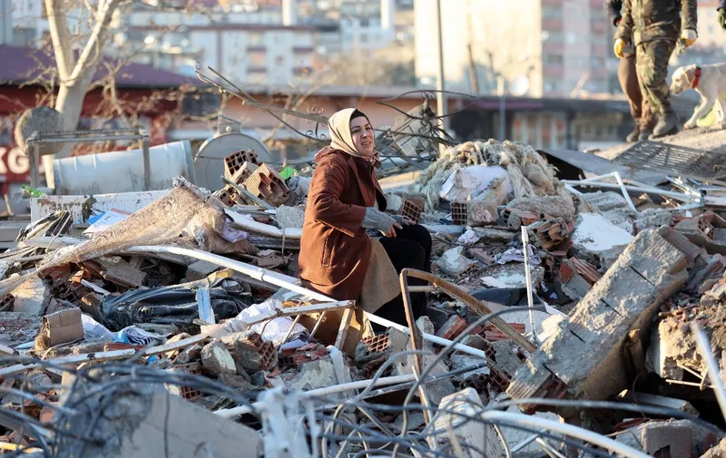 A woman sits on the rubble of a destroyed building in Kahramanmaras, southern Turkey, a day after a 7.8-magnitude earthquake struck the country's southeast, on February 7, 2023. - Rescuers in Turkey and Syria braved frigid weather, aftershocks and collapsing buildings, as they dug for survivors buried by an earthquake that killed more than 5,000 people. Some of the heaviest devastation occurred near the quake's epicentre between Kahramanmaras and Gaziantep, a city of two million where entire blocks now lie in ruins under gathering snow. (Photo by Adem ALTAN / AFP)