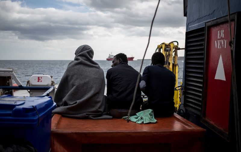 Three of the 47 rescued migrants aboard the Dutch-flagged Sea Watch 3 NGO vessel, sit on the ship's half-deck on January 30, 2019 off Syracuse, Sicily. - 47 rescued migrants aboard the Sea Watch NGO vessel were expected to disembark in Catania after Italy and France, Germany, Malta, Portugal, Romania and Luxembourg agreed to take them in. The fate of the migrants has been at the centre of a standoff between Italy's far-right Deputy Prime Minister Matteo Salvini -- who has closed the ports to migrants and demanded Europe take its share -- and the German NGO Sea Watch. (Photo by FEDERICO SCOPPA / AFP)