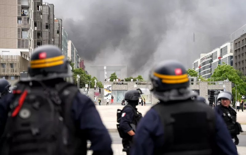 CRS riot police face protesters, with the "Grande Arche de la Defense" seen in the background, at the end of a commemoration march for a teenage driver shot dead by a policeman, in the Parisian suburb of Nanterre, on June 29, 2023. Violent protests broke out in France in the early hours of June 29, 2023, as anger grows over the police killing of a teenager, with security forces arresting 150 people in the chaos that saw balaclava-clad protesters burning cars and setting off fireworks. Nahel M., 17, was shot in the chest at point-blank range in Nanterre in the morning of June 27, 2023, in an incident that has reignited debate in France about police tactics long criticised by rights groups over the treatment of people in low-income suburbs, particularly ethnic minorities. (Photo by Zakaria ABDELKAFI / AFP)