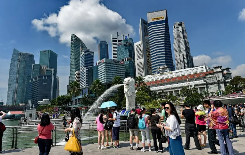 Tourists visit Singapore's famous Merlion (C) in front of the skyline of the city's financial business district on February 25, 2015.  Singapore on February 23 announced income tax rises for the top five percent of the population to fund rising social spending targeted at the poor and elderly in the rapidly ageing city-state.    AFP PHOTO / ROSLAN RAHMAN