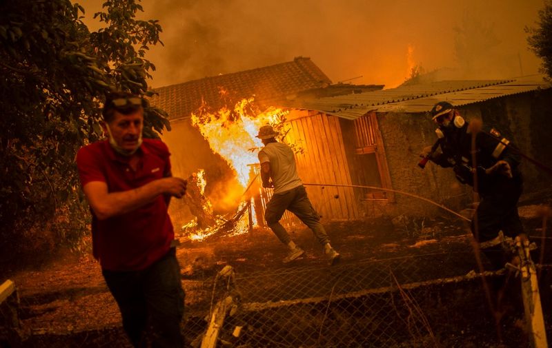 A firefighter and locals rush to a burning house in an attempt to extinguish forest fires that are approaching the village of Pefki on Evia (Euboea) island, Greece's second largest island, on August 8, 2021. - Hundreds of Greek firefighters fought desperately on August 8 to control wildfires on the island of Evia that have charred vast areas of pine forest, destroyed homes and forced tourists and locals to flee. Greece and Turkey have been battling devastating fires for nearly two weeks as the region suffered its worst heatwave in decades, which experts have linked to climate change. (Photo by ANGELOS TZORTZINIS / AFP)