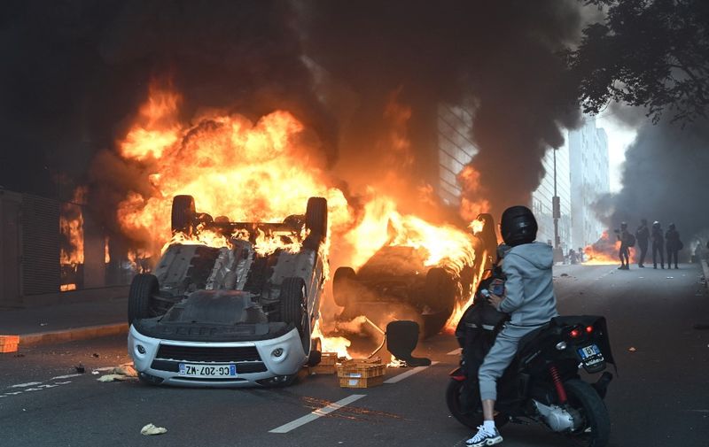 A photo shows cars burning in the street at the end of a commemoration march for a teenage driver shot dead by a policeman, in the Parisian suburb of Nanterre, on June 29, 2023. Violent protests broke out in France in the early hours of June 29, 2023, as anger grows over the police killing of a teenager, with security forces arresting 150 people in the chaos that saw balaclava-clad protesters burning cars and setting off fireworks. Nahel M., 17, was shot in the chest at point-blank range in Nanterre in the morning of June 27, 2023, in an incident that has reignited debate in France about police tactics long criticised by rights groups over the treatment of people in low-income suburbs, particularly ethnic minorities. (Photo by Bertrand GUAY / AFP)