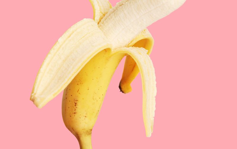Half peeled banana on a pink background.