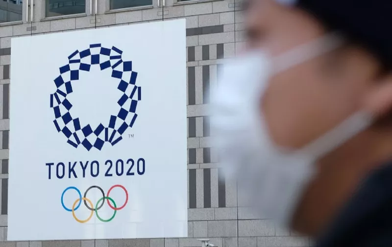 (FILES) In this file photo taken on March 19, 2020 a man wearing a mask passes the logo of the Tokyo 2020 Olympic Games displayed on the Tokyo Metropolitan Government building. - Senior International Olympic Committee (IOC) official Dick Pound said March 23, 2020 a postponement of this year's Tokyo Olympics is now inevitable as the world reels from the coronavirus pandemic. (Photo by Kazuhiro NOGI / AFP)