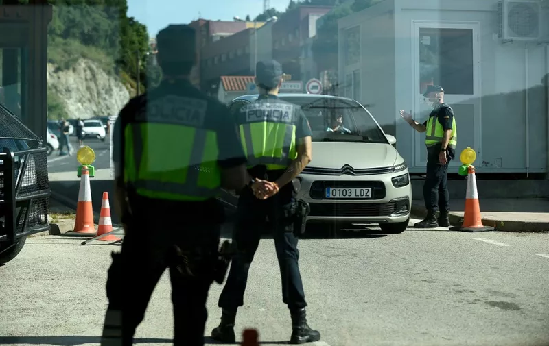 Spanish border police officers stand guard at a checkpoint as a car crosses the French-Spanish border at La Jonquera on June 21, 2020. - Traffic flowed again across Spain's border with France as the last of the strict Spanish coronavirus restrictions introduced in March were eased. (Photo by Josep LAGO / AFP)