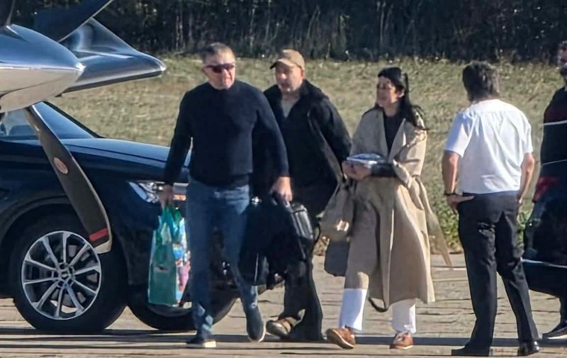 Troje ljudi s torbama hoda uz crni automobil i privatni zrakoplov na pisti, a pilot ih dočekuje.