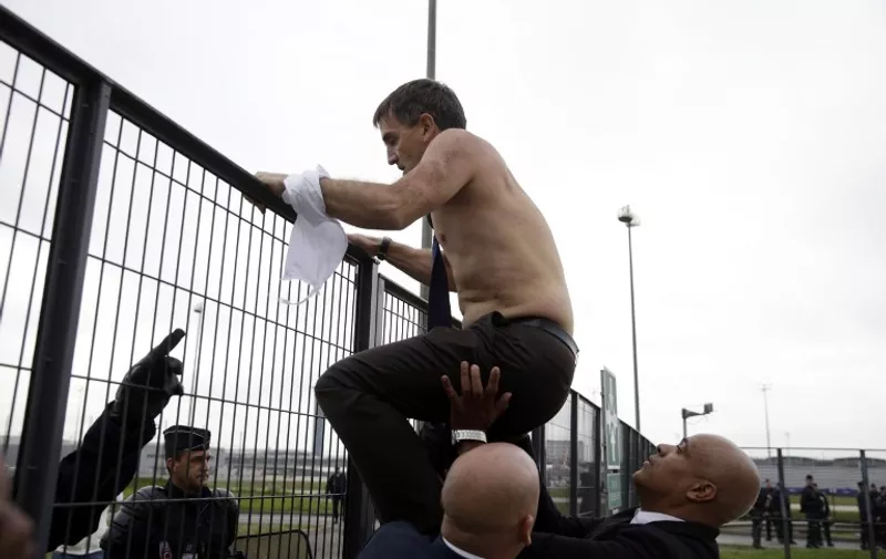 Human Resources Director of Air France Xavier Broseta, shirtless, tries to cross a fence, helped by security and police officers, after several hundred of employees invaded the offices of Air France, interrupting the meeting of the Central Committee (CCE) in Roissy-en-France, on October 5, 2015. Air France-KLM unveiled a revamped restructuring plan on October 5 that could lead to 2,900 job losses after pilots for the struggling airline refused to accept a proposal to work longer hours. AFP PHOTO / KENZO TRIBOUILLARD