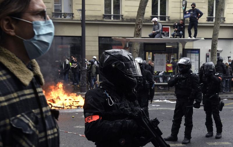 A police officer of the brigade of repression of violent action BRAV holds a brigade of repression of violent action BRAV 40 millimetre rubber defensive bullet launcher (LBD 40) near a fire burning in the street during the annual May Day (Labour Day) rally in Paris on May 1, 2021. (Photo by Bertrand GUAY / AFP)