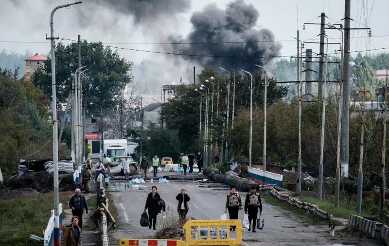 A woman (3rd R), evacuating with belongings, protects her ears after an explosion on a bridge over the Oskil River as black smoke rises in the frontline city of Kupiansk, Kharkiv region, on September 24, 2022, amid the Russian invasion of Ukraine. In the northeastern town of Kupiansk, which was recaptured by Ukrainian forces, clashes continued with the Russian army entrenched on the eastern side of the Oskil River. (Photo by Yasuyoshi CHIBA / AFP)