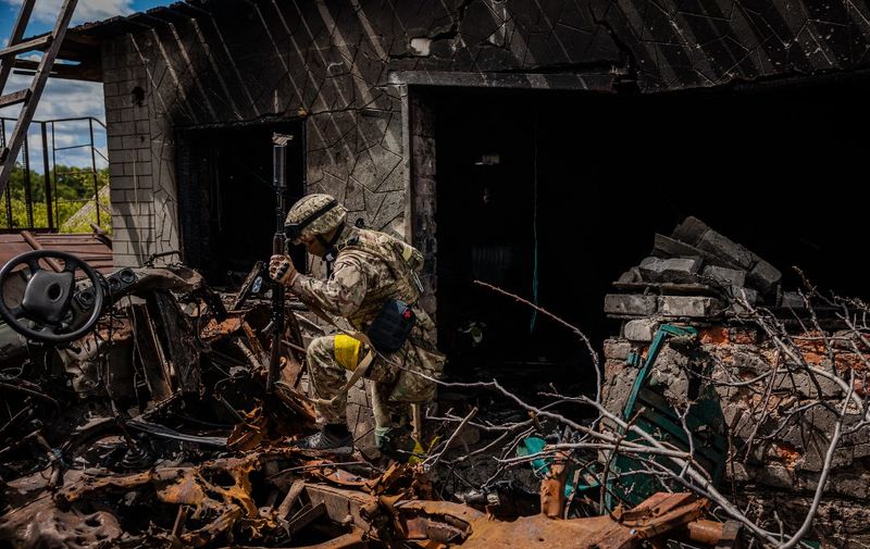 A soldier of the Kraken Ukrainian special forces unit walks past wreckage in the village of Rus'ka Lozova, north of Kharkiv, on May 16, 2022. - Ukraine has said its troops have regained control of territory on the Russian border near the country's second-largest city of Kharkiv, which has been under constant fire since Moscow's invasion began. (Photo by Dimitar DILKOFF / AFP)