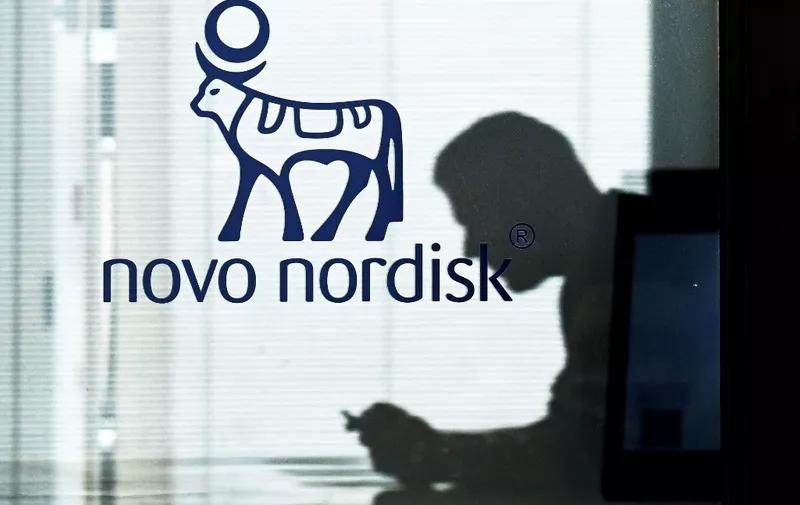An employee sits next to a door bearing the logo of Novo Nordisk at the factory in Hilleroed on September 26, 2023. Novo Nordisk is a leading global healthcare company, founded in 1923 and headquartered in Denmark, aiming to defeat diabetes and other serious chronic diseases such as obesity and rare blood and endocrine disorders. On June 12, 2023, the company announced plans to invest 15.9 billion Danish kroner to expand an existing Active Pharmaceutical Ingredient (API) production facility in the country. (Photo by Sergei GAPON / AFP)