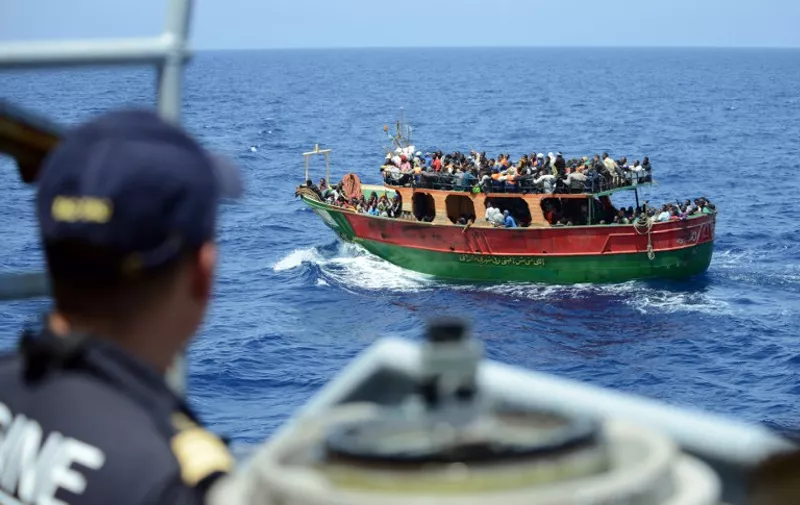 This handout picture taken and released by the French Navy (Marine Nationale) on May 20, 2015 shows a member of the French Navy crew of the Commandant Birot patrol looking at migrants aboard the Afandina fishing boat, during a rescue operation of the 297 migrants, in the Mediterranean Sea, some 300km southeast of Italy. Members of the French Navy, part of the European Union's Mediterranean Triton operation, rescued 297 migrants on May 20, including 51 women and children, the French maritime prefecture said.  AFP PHOTO / MARINE NATIONALE
= RESTRICTED TO EDITORIAL USE - MANDATORY CREDIT "AFP PHOTO / MARINE NATIONALE" - NO MARKETING NO ADVERTISING CAMPAIGNS - DISTRIBUTED AS A SERVICE TO CLIENTS =