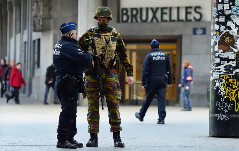 A Belgian soldier speaks to a police officer outside Brussels Central Station as people are allowed in small groups of ten to reach the station in order to take their commuter train following attacks in Brussels on March 22, 2016. 
Airlines cancelled hundreds of flights and European railways froze links with Brussels after a series of bombs blasts killed around 35 people in the city's airport and a metro train, sparking a broad security response. / AFP / EMMANUEL DUNAND