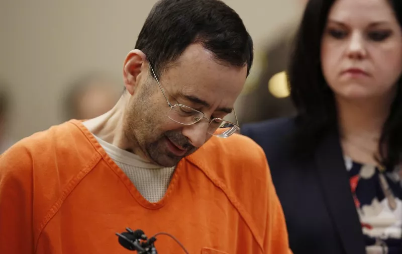 Former Michigan State University and USA Gymnastics doctor Larry Nassar (L) reacts to defense attorney Shannon Smith (R) reading the charges he pled to in Ingham County Circuit Court on November 22, 2017 in Lansing, Michigan. - Former USA Gymnastics team doctor Lawrence (Larry) Nassar, accused of molesting dozens of female athletes over several decades, on Wednesday pleaded guilty to multiple counts of criminal sexual conduct. Nassar -- who was involved with USA Gymnastics for nearly three decades and worked with the country's gymnasts at four separate Olympic Games -- could face at least 25 years in prison on the charges brought in Michigan. (Photo by JEFF KOWALSKY / AFP)