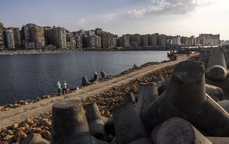 People fish with rods near the concrete blocks installed to break the Mediterranean sea waves along the waterfront in Egypt's northern Mediterranean coastal city of Alexandria on October 31, 2022. (Photo by Khaled DESOUKI / AFP)