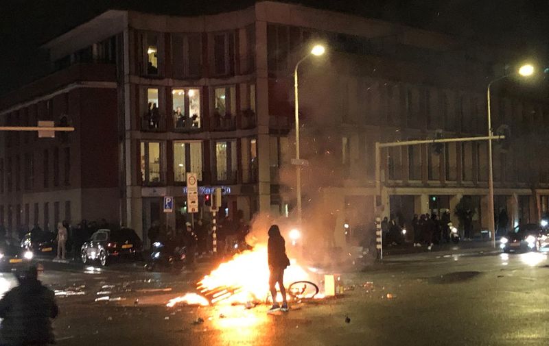 A man walks in front of a fire in a street of The Hague during a demonstration against the Dutch government's coronavirus measures, on November 20, 2021. - Fresh rioting broke out late November 20 over the Dutch government's coronavirus measures, with rioters pelting police with stones and fireworks as protests turned violent for a second night in the Netherlands. (Photo by Danny KEMP / AFP)