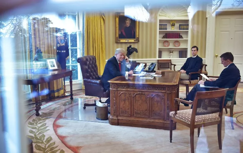 US President Donald Trump(L)seen through an Oval Office window speaks on the phone to King Salman of Saudi Arabia, watched by Senior Advisor Jared Kusher(C), and National Security Michael Flynn, in the Oval Office of the White House on January 29, 2017 in Washington, DC.
Trump is to speak by phone with the leaders of Saudi Arabia and the United Arab Emirates on January 29, 2017, amid an uproar over his travel ban for some Muslim majority countries. Trump also will talk to the acting president of South Korea, Hwang Kyo-Ahn, the White House said Saturday in a brief statement.
 / AFP PHOTO / MANDEL NGAN